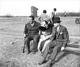 Man holding rifle or shotgun, with a man and woman possibly at a shooting range circa 1936.