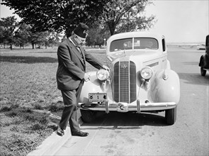 Shriner L.P. Steuart standing by car, pointing at personalized license plate circa 1935.