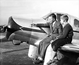 Man and his son sitting on the wing of a Curtiss airplane circa 1936.