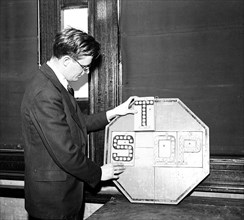 Man inserting a letter T into a stop sign with reflectors on it circa 1936.