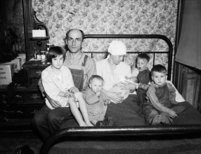 Poor family of a husband and wife with five children on a bed circa 1936.