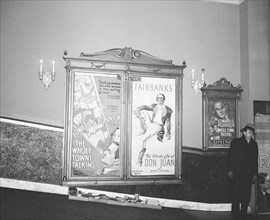Man standing in movie theater lobby next to movie posters circa 1935.