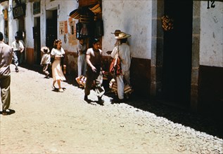 Locals walking down a street in a city in Mexico circa 1950-1955.