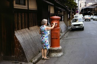Woman mailing letters in a postal service mailbox in Kyoto Japan circa 1976.