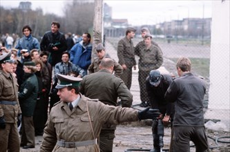 An East German policeman motions to the crowd as the Berlin Wall is dismantled at Potsdamer Platz..