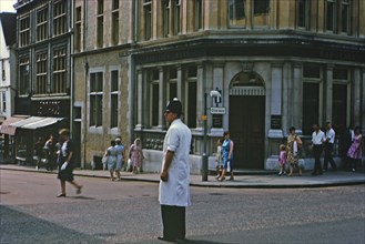 Bobby in London standing in the middle of a street in front of a Barclays Bank Building circa 1970.