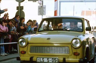 West German children applaud as an East German couple drive through Checkpoint Charlie and take advantage of relaxed travel restrictions to visit West Germany..