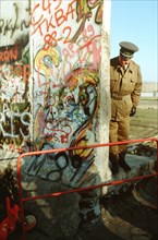 An East German policeman looks at a small Christmas tree adorning the West German side of the Berlin Wall.  The guard is standing at the newly created opening in the Berlin Wall at Potsdamer Platz..