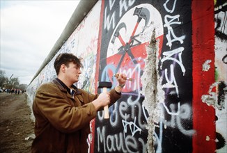 A West German man uses a hammer and chisel to chip off a piece of the Berlin Wall as a souvenir.  A portion of the Wall has already been demolished at Potsdamer Platz..