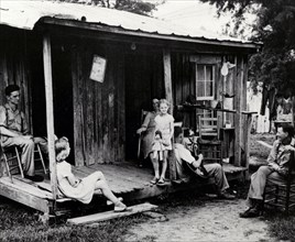 A rural family sits on an unscreened porch in the early evening