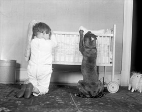 A small child and a large dog kneeling and praying beside a crib