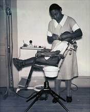 African American dentist is working on a patient's teeth in a sparsely furnished office.