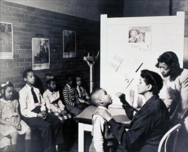 Interior view of a childrens' health clinic; an African American child is having his throat examined.
