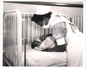 A nurse is leaning over a newborn in a crib.