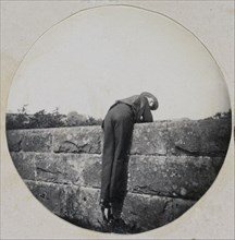 Man in Hat Bent Over a Stone Wall