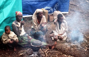 Refugee family sits near a smoldering fire in the camp near Goma
