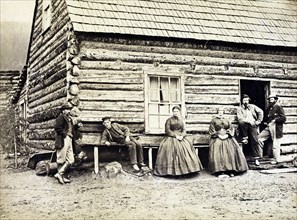 Frontier family outside their log cabin