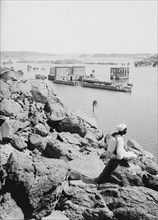 General view of Island of Philae, man sitting on a rock, looking at water ca. 1900