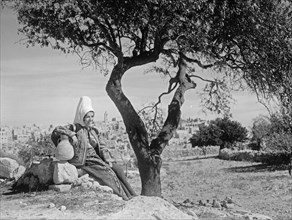 Bethlehem woman with jar seated under almond tree. Bethlehem in background ca. between 1934 and 1939