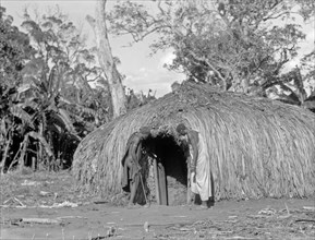 1930s Tanganyika / Tanzania - Two men looking into the entrance of a typical native straw hut  ca. 1936
