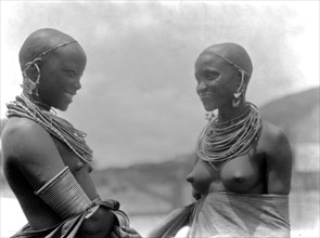 Two Longido girls sharing conversation, wearing traditional rings and no clothes ca. 1936
