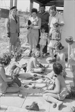Children of the settlement of Gat (modern day Kibbutz) busy polishing their shoes as adults watch them ca. 1946