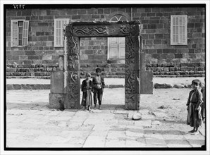 Children standing beneath an ornamented doorway on the town square in Kanawat. Carving of grapevine pattern ca. 1938