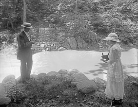 Woman photographing man in woodland setting ca.  between 1910 and 1920