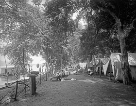People camping out by a river or canal, possibly around the 4th of July, note the American flags ca.  between 1910 and 1935