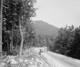 Men standing outside a car on a rural road ca.  between 1910 and 1926