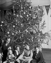 Children sitting in front of a Christmas tree with their parents ca.  between 1910 and 1925