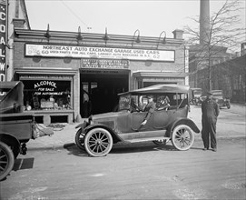 Man in a car outside the North East Auto Exchange used car dealership and garage ca.  between 1910 and 1926