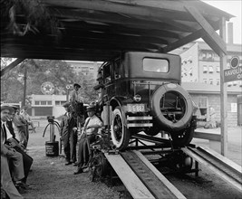 Men standing next to a car on a rack at a Havoline Oil Company station ca.  between 1910 and 1935