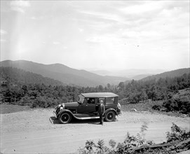 Man standing outside his automobile on a rural mountain road  ca.  between 1910 and 1926