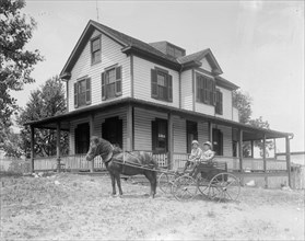 Children in horse-drawn wagon in front of house. ca.  between 1910 and 1920