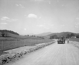 Two men standing outside an automobile on a rural road ca.  between 1910 and 1926