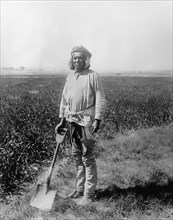 Native American man holding a shovel next to a field ca. between 1910 and 1935