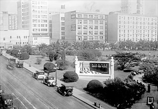 Cars parked in road near a bulletin board donated to U.S. Food Administration by Foster & Kleiser ca.  between 1910 and 1935