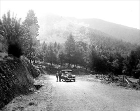 Men stand outside a car on a rural road in the mountains ca.  between 1910 and 1926