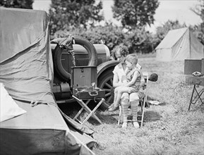 Woman and child at a campsite listening to a portable phonograph ca. between 1909 and 1923