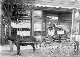 Man sitting in a horse drawn wagon in front of a store ca. between 1909 and 1923