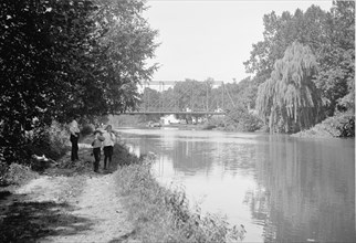 Kids fishing in the C&O canal, the Chain Bridge in the background ca. between 1909 and 1923