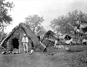 Father and children outside straw cottages, Salmanca Meixco ca. between 1909 and 1920
