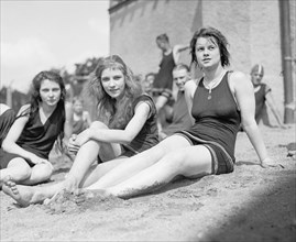 Three young women or teen girls sitting on a beach ca. between 1909 and 1932