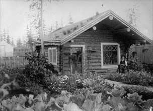 Man sitting on his porch outside his cottage & garden, Alaska ca. between 1909 and 1920