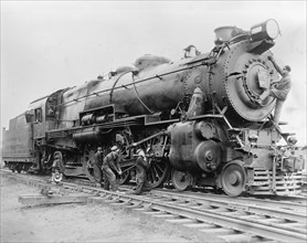 Workers conducting maintenance on a train locomotive ca. between 1909 and 1940