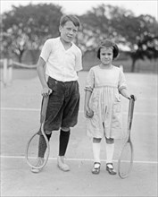 Jack & Peggy Baker on a tennis court holding racquets ca.  between 1918 and 1920