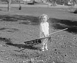 A young toddler girl holding a rake ca.  between 1918 and 1920