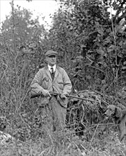 Miles Poindexter holding a shotgun (or rifle) with his hunting dog  ca.  between 1918 and 1920