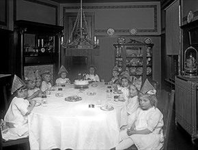 Girls sit around a table with lit birthday cake at six year old children's birthday party ca.  between 1918 and 1928